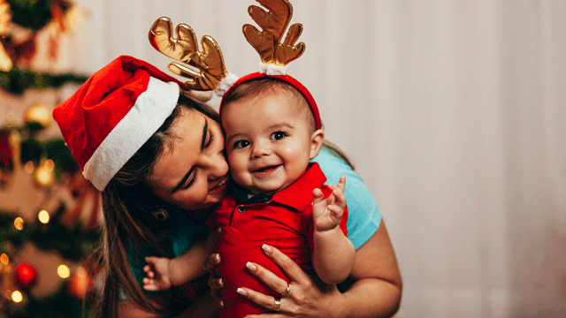 一位妈妈亲她十二月宝宝脸颊前的圣诞树