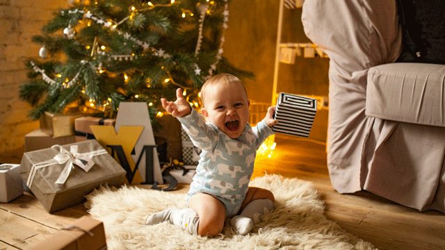 婴儿在圣诞树前欢笑时,他举着礼物