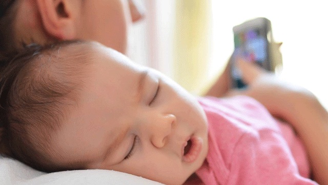 婴儿睡在母亲的肩上,同时检查手机