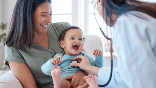 婴儿用听波器对医生笑 坐在医生办公室妈妈大腿上
